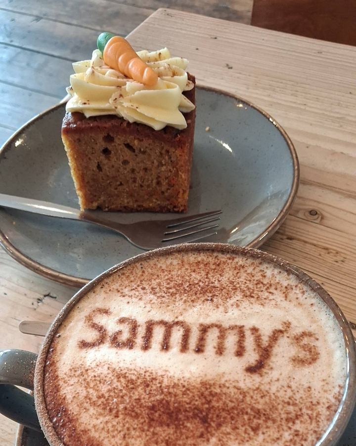 A cappuccino with Sammy’s dusted in cocoa on the foam, beside a slice of carrot cake topped with a marzipan carrot