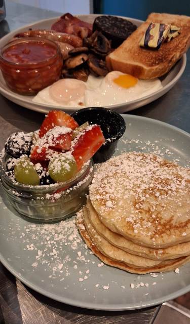A stack of pancakes dusted with icing sugar beside a pot of mixed berries